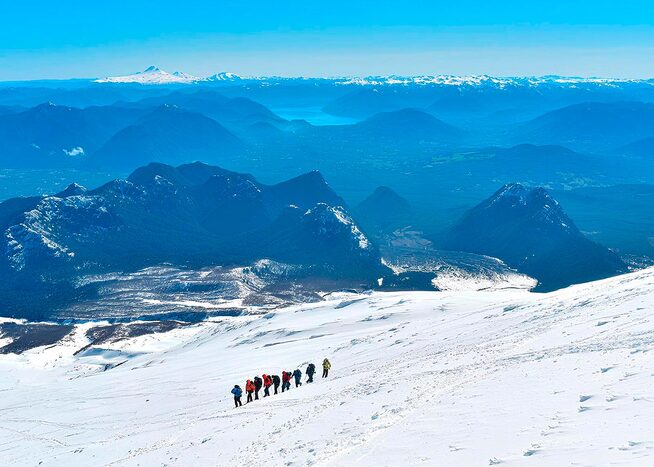 People ascending Villarrica Volcano with a panoramic view of snowy mountains and valleys in southern Chile.