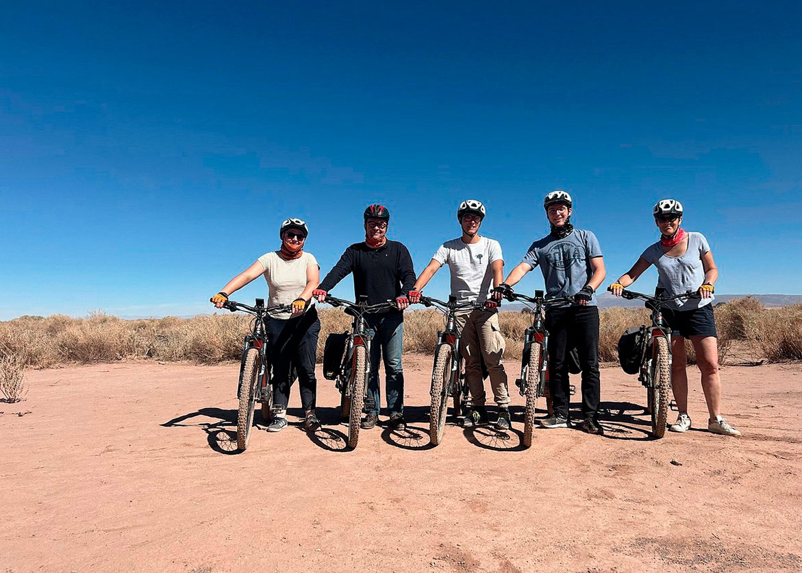 Group of cyclists with e-bikes posing in the desert of San Pedro de Atacama under a clear sky.