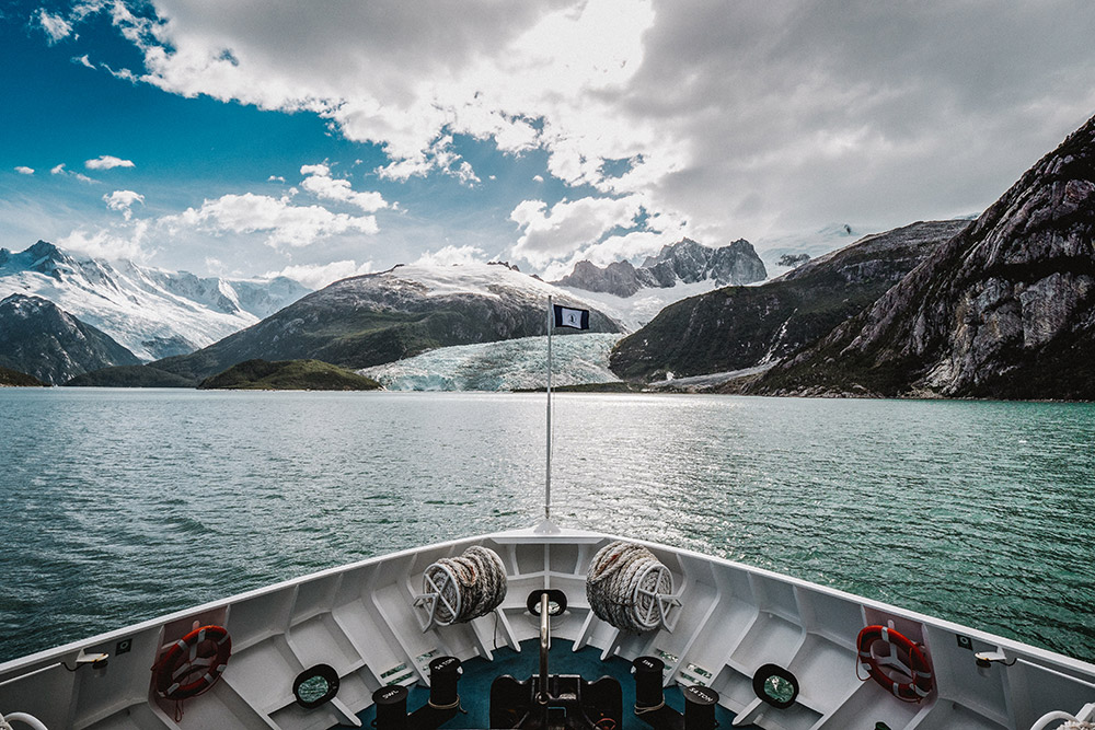 Cruise sailing through the fjords of Tierra del Fuego with a view of the glacier and snow-capped mountains of Alberto de Agostini National Park, Chile.
