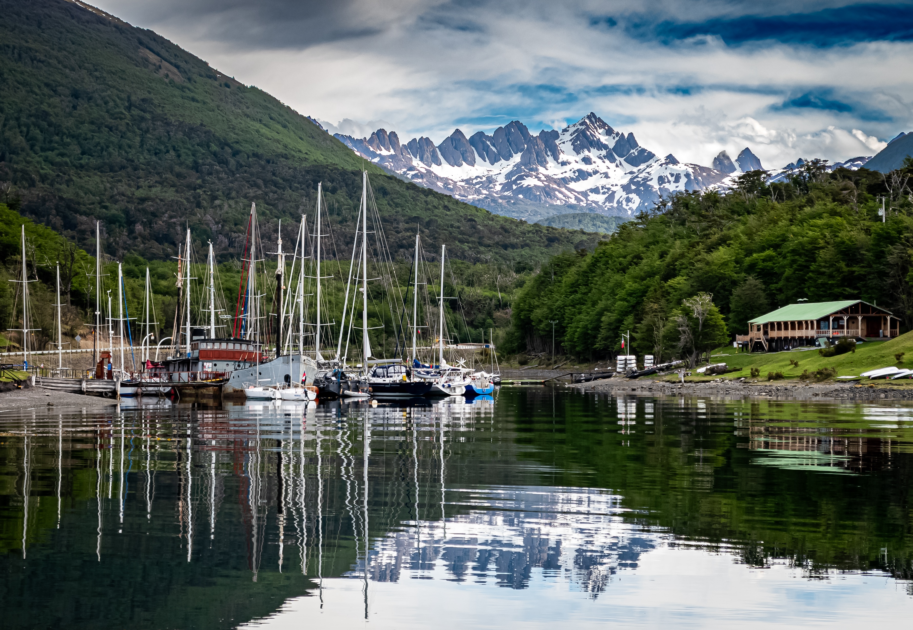 Puerto Williams in Chilean Patagonia with sailboats anchored in the Beagle Channel, surrounded by green forests and with the Dientes de Navarino Range in the background covered in snow.