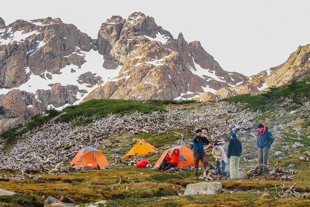 Group of hikers camping in the Dientes de Navarino Circuit, with orange tents facing snowy mountains in Chilean Patagonia.