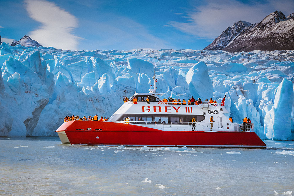 Catamaran Grey III sailing in front of the Grey Glacier in Torres del Paine, with passengers observing the blue ice walls of Chilean Patagonia.