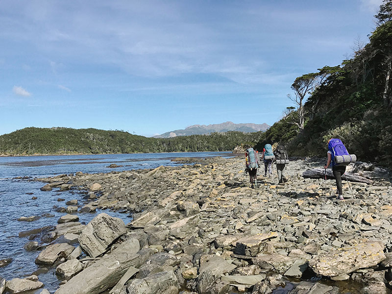 Group of hikers trekking along the rocky coast of Cabo Froward in Chilean Patagonia, with trekking backpacks