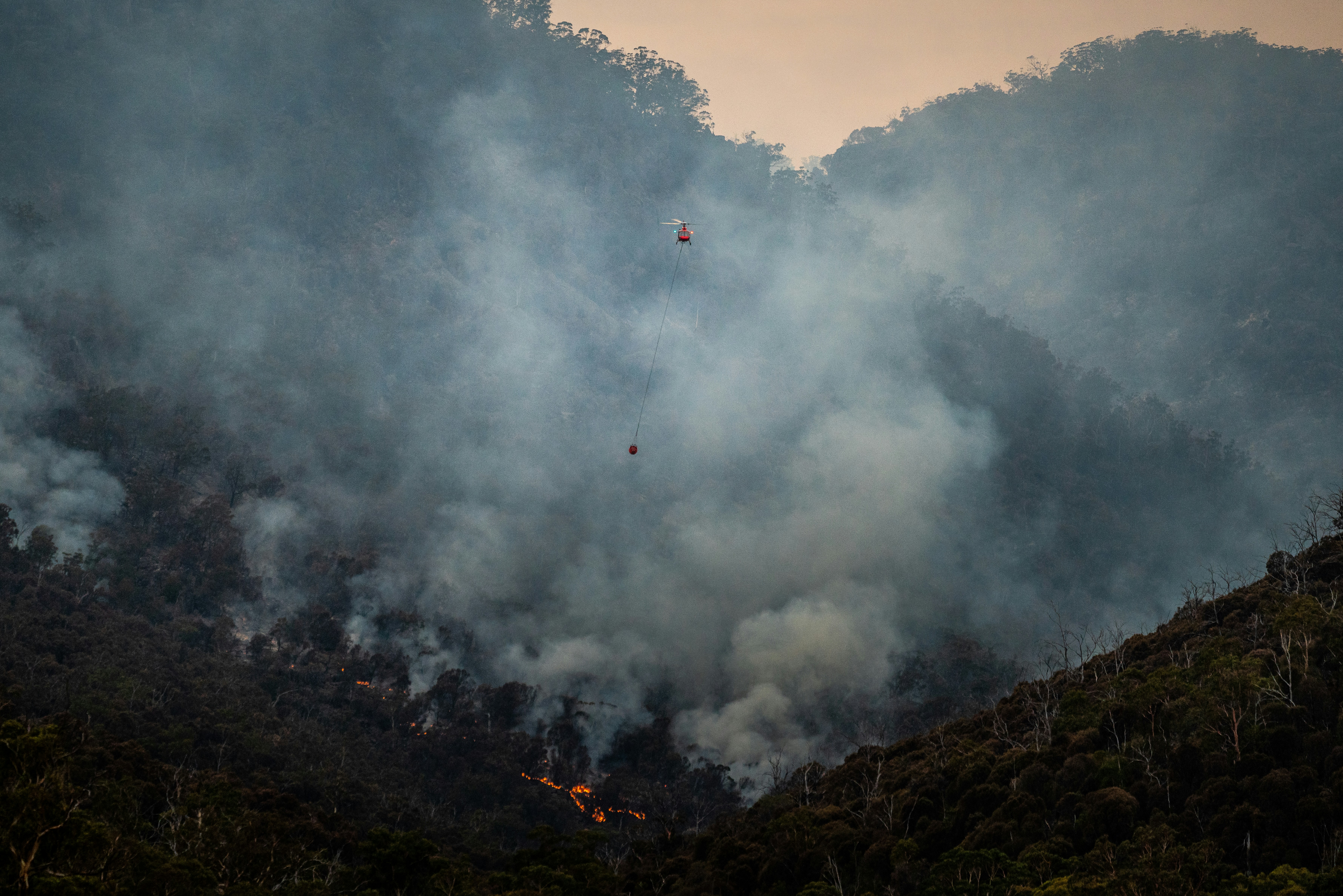 Helicopter combating a wildfire from the air, over a forest covered in smoke