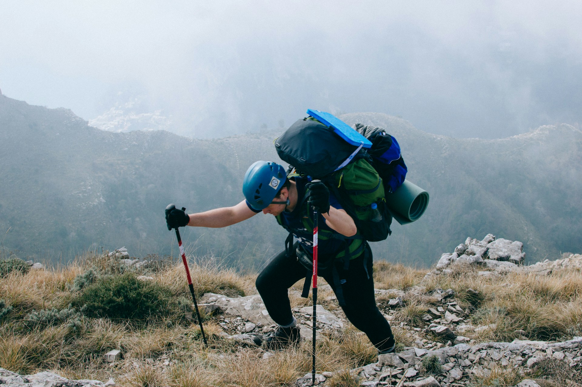 Hiker ascending with a heavy backpack and trekking poles on challenging mountain terrain.
