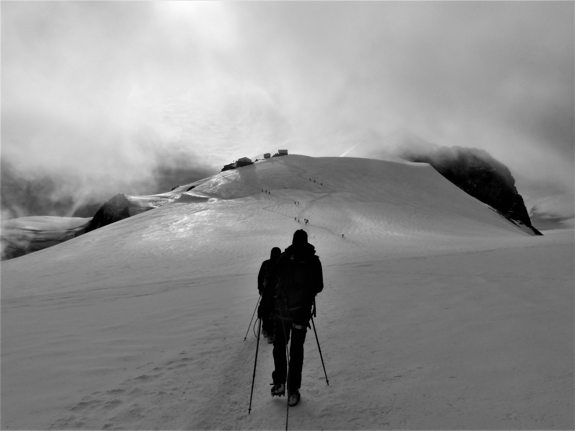 Hikers ascending a snowy mountain with trekking poles in high mountain conditions.