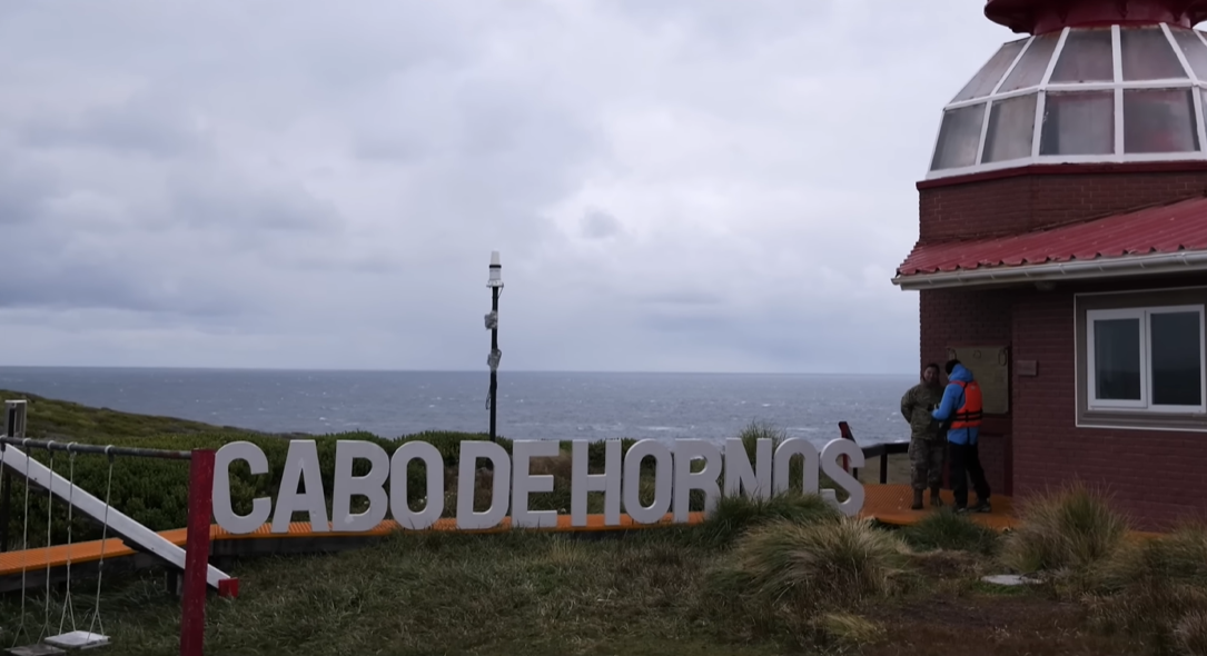 Tourists next to the lighthouse and the Cape Horn sign during an expedition to the end of the world.