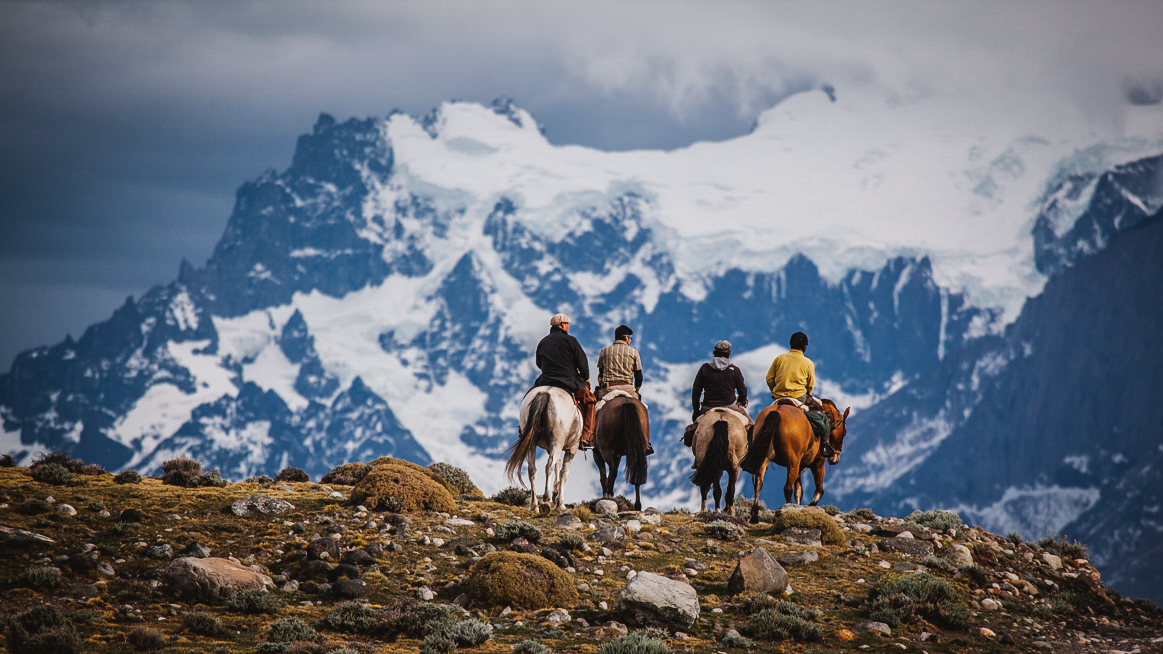 Group of riders horseback riding in Patagonia in front of snowy mountains, in a natural high mountain landscape