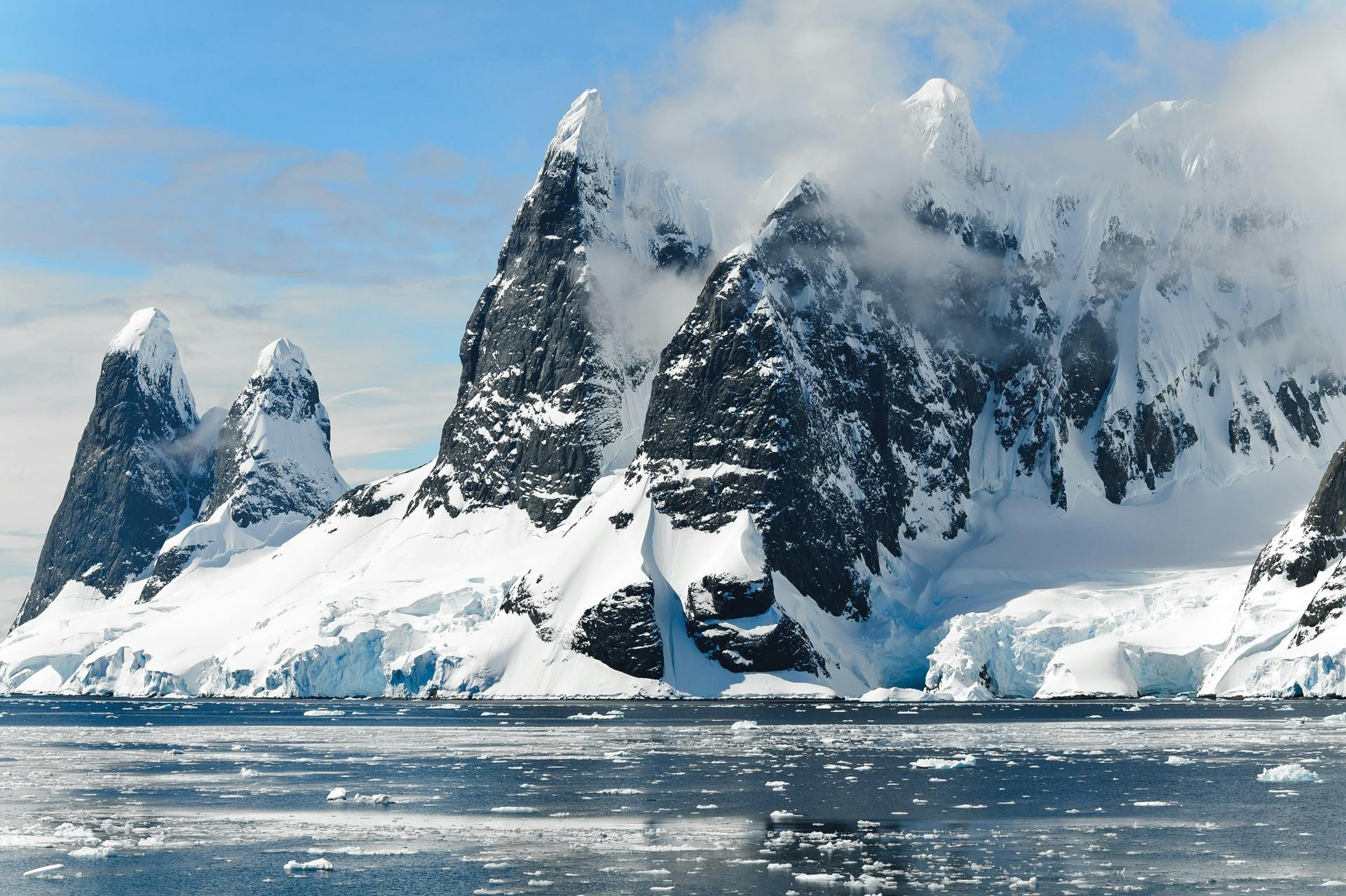 Impressive rocky mountains covered in snow and glaciers on the coast of Antarctica, with ice blocks floating on the frozen sea.