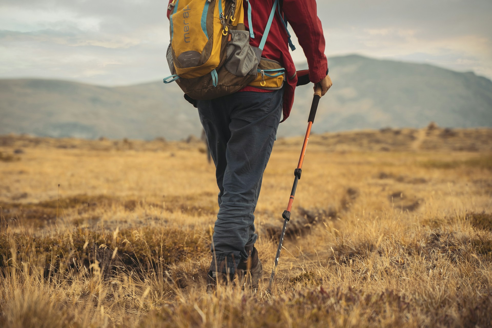 Hiker walking with trekking poles and a backpack in an open mountain landscape.